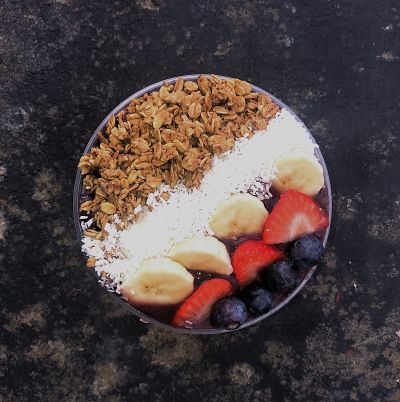 Acai bowl with granola, coconut, banana, strawberries, and blueberries in stripes on top