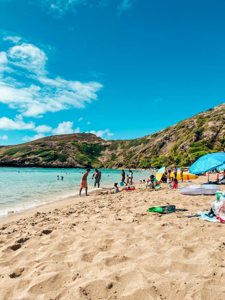 Beach in Oahu with people playing in the water and the sand. Jungle hill in the background