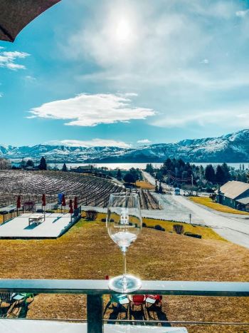 Wine glass on a ledge with a grass lawn and Lake Chelan in the background