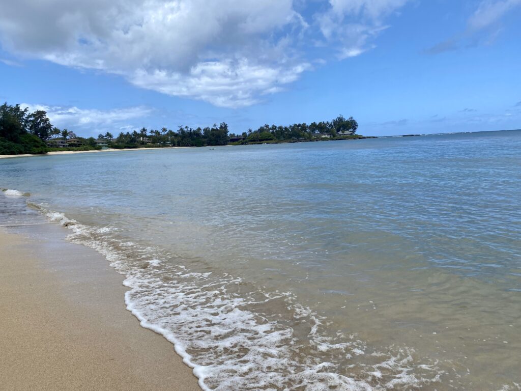 view down the waterline of Kawela bay in Oahu with half sand and half ocean