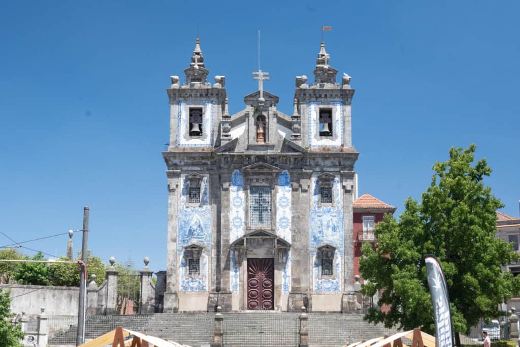 The Church of Saint Ildefonso in Porto, Portugal, with its distinctive blue and white azulejo tile panels depicting religious scenes, stands proudly under a clear blue sky.