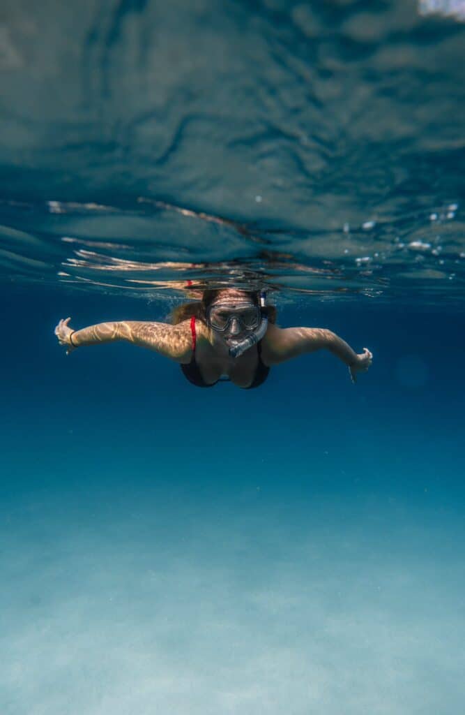 Unrecognizable female tourist in goggles and snorkeling mask swimming in clear blue sea during summer vacation