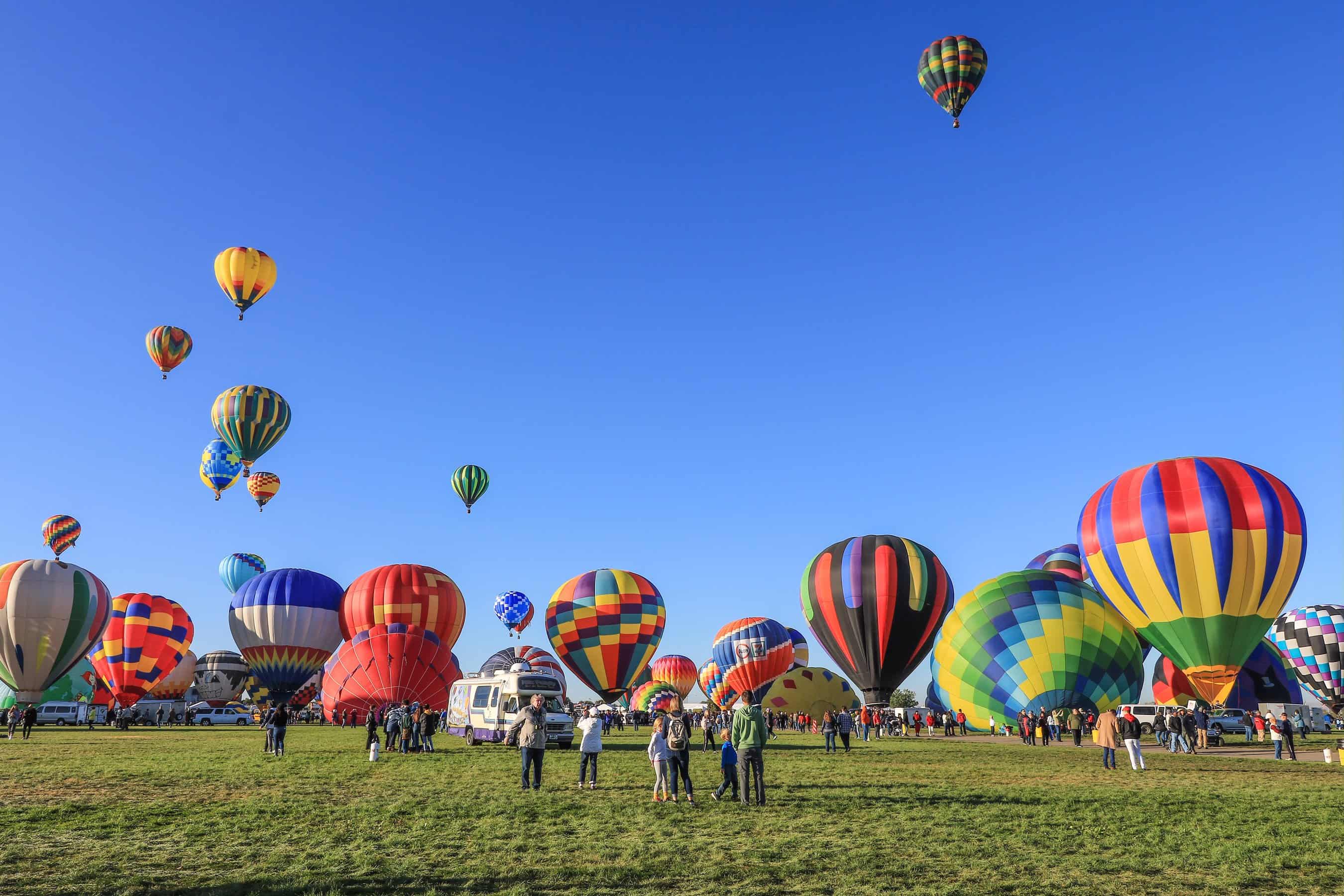 A festive scene at the Albuquerque International Balloon Fiesta in New Mexico, with a vibrant array of hot air balloons rising against a clear blue sky as onlookers marvel at the spectacle.