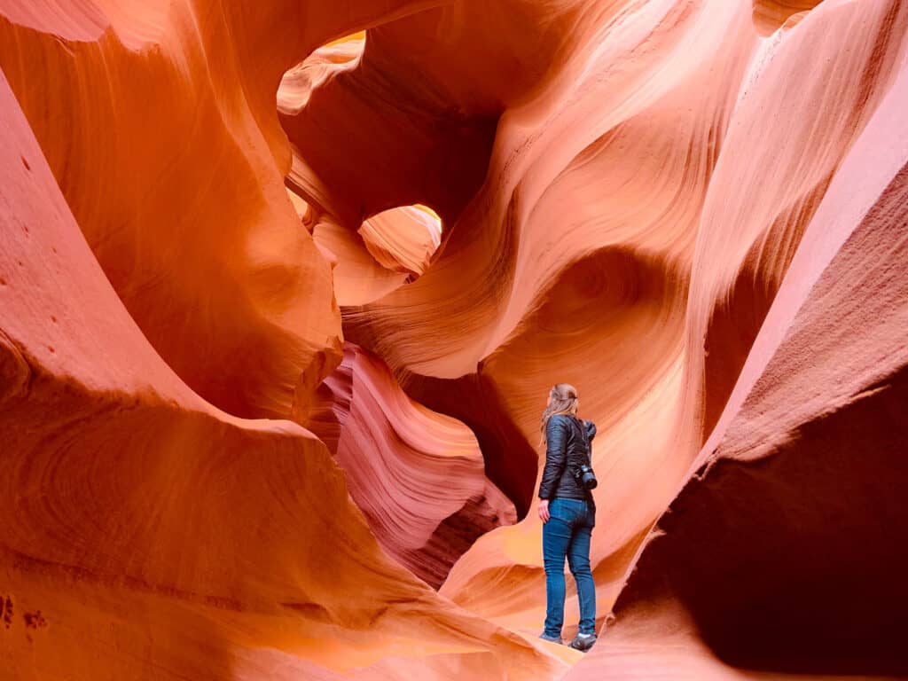 A visitor in silhouette stands captivated by the smooth, swirling orange walls of Antelope Canyon in Arizona, illustrating the natural artistry of wind-eroded sandstone.