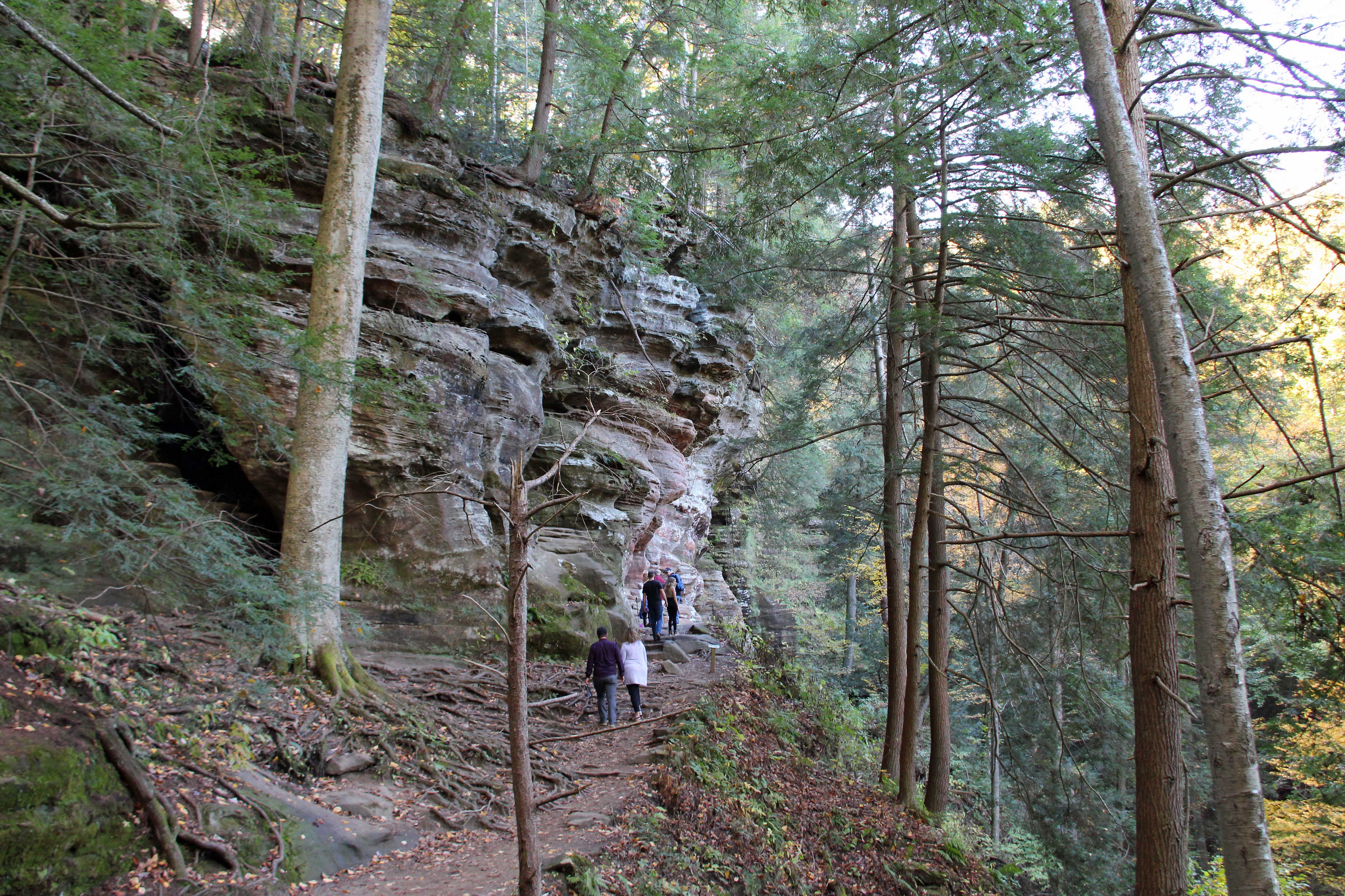 Visitors hiking a wooded trail along the impressive rock formations at Hocking Hills State Park, showcasing the natural beauty and serene environment
