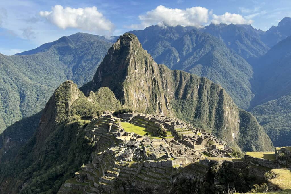 The ancient Incan citadel of Machu Picchu in Peru, set high in the Andes Mountains, with its well-preserved ruins and terraces, highlighted by the dramatic backdrop of steep, lush peaks and a clear sky above.