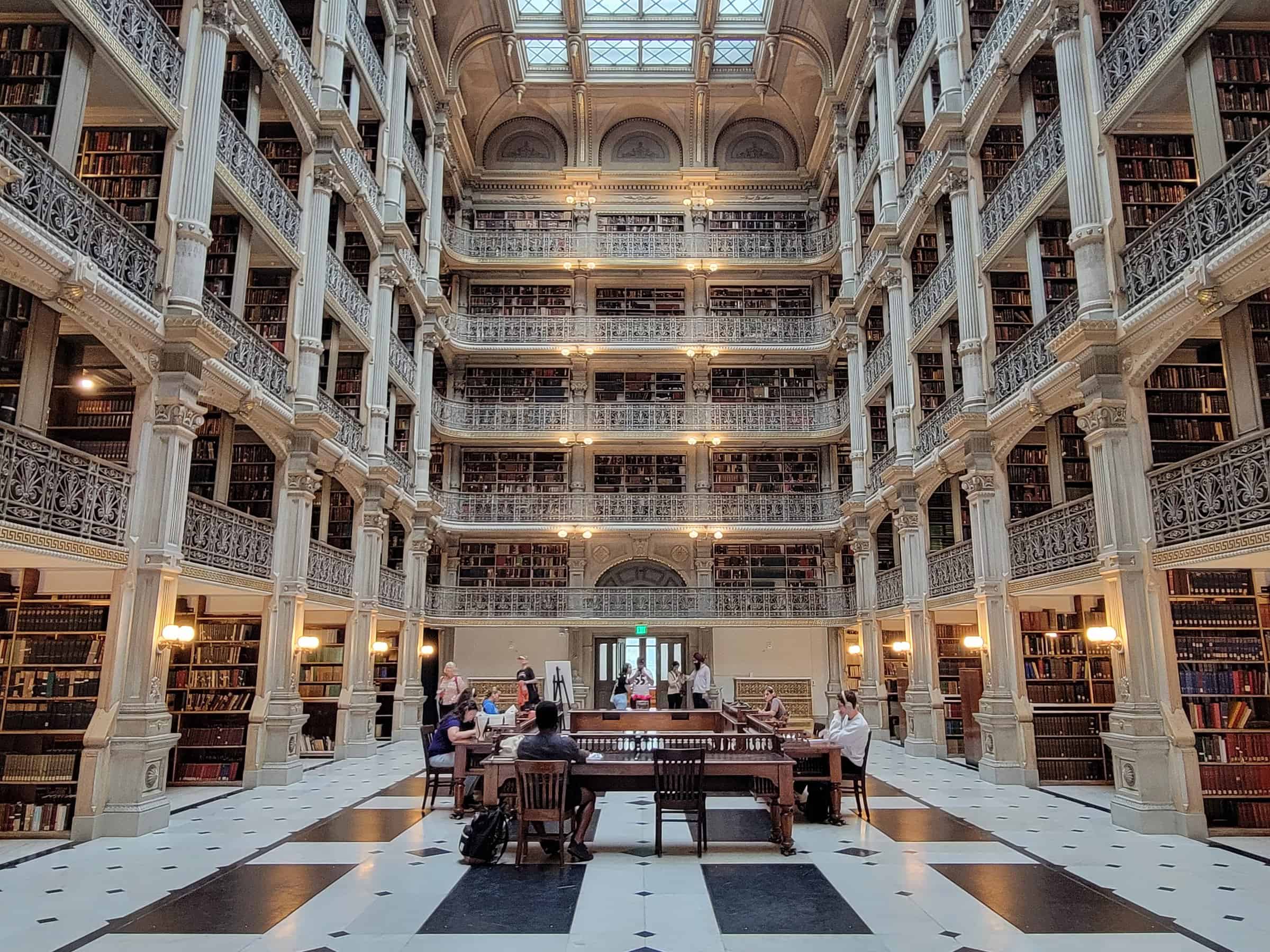 Interior of the George Peabody Library in Baltimore, showcasing its grand five-tiered, cast-iron balconies filled with books, ornate railings, and patrons enjoying the reading space