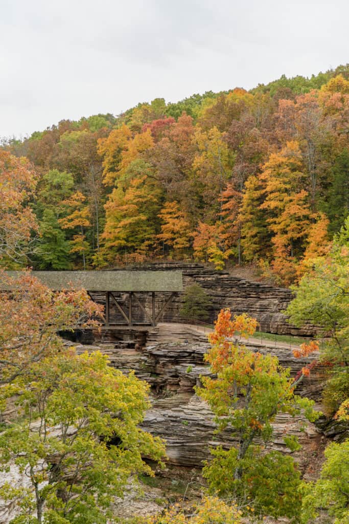 Autumn colors paint a vibrant scene at the Top of the Rock in Branson, Missouri, with a rustic wooden bridge crossing over layered rock formations amidst the foliage.