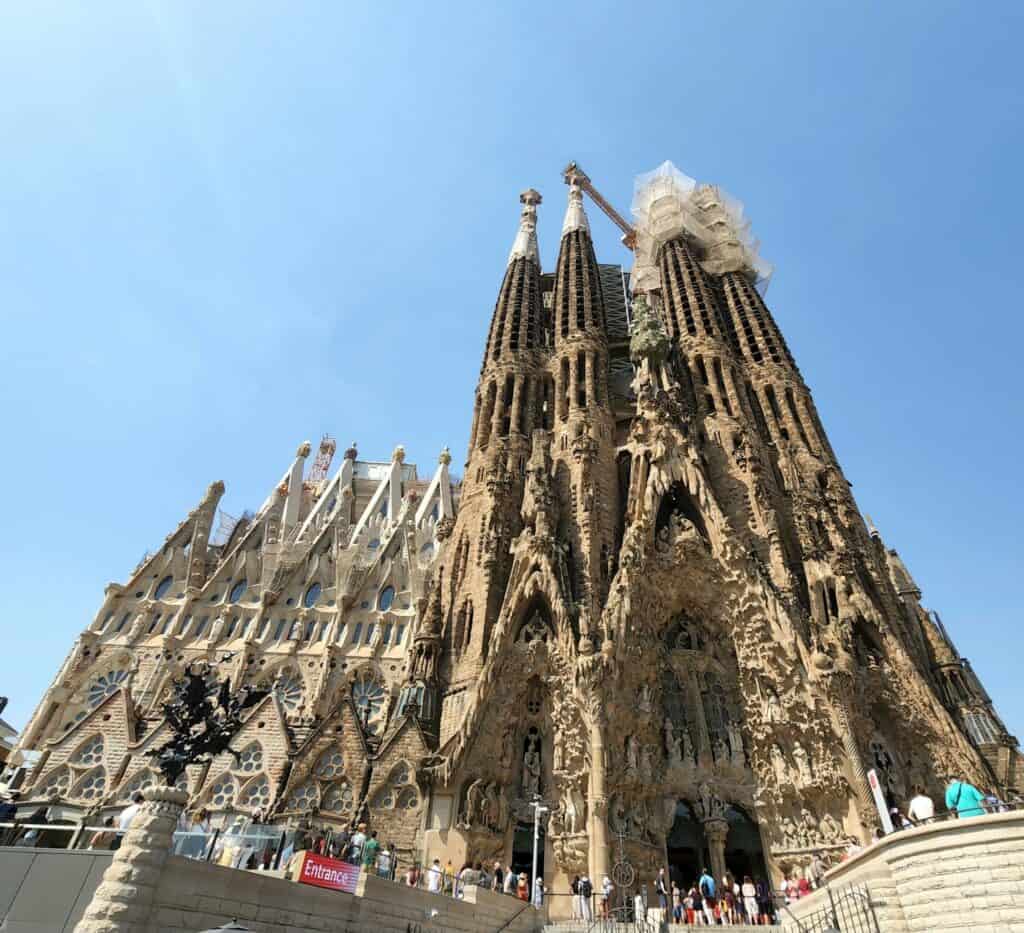 The imposing façade of La Sagrada Familia in Barcelona, displaying its intricate Gothic and Art Nouveau details, with construction cranes towering above as part of the ongoing work on this architectural masterpiece by Antoni Gaudí.