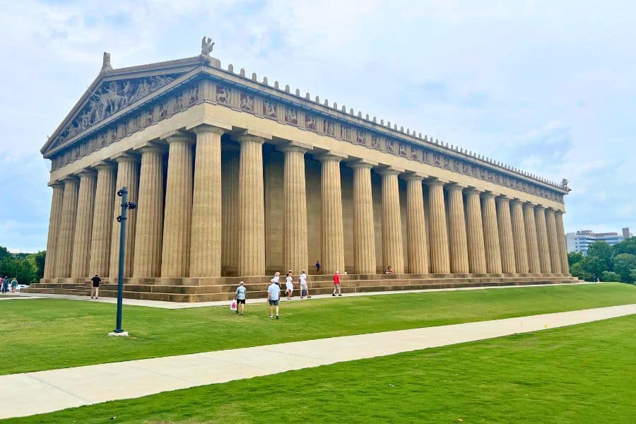The Parthenon replica in Centennial Park, Nashville, Tennessee, showcasing its imposing columns and intricate pediments. Visitors can be seen walking on the paths around this full-scale monument on a day with overcast skies