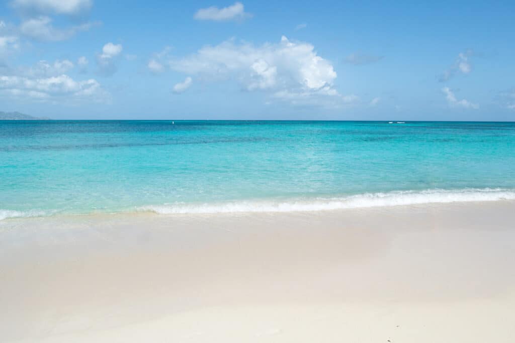 Pristine white sandy beach of St. Croix with crystal-clear aquamarine waters meeting the horizon under a blue sky dotted with fluffy clouds, embodying a tranquil tropical paradise.