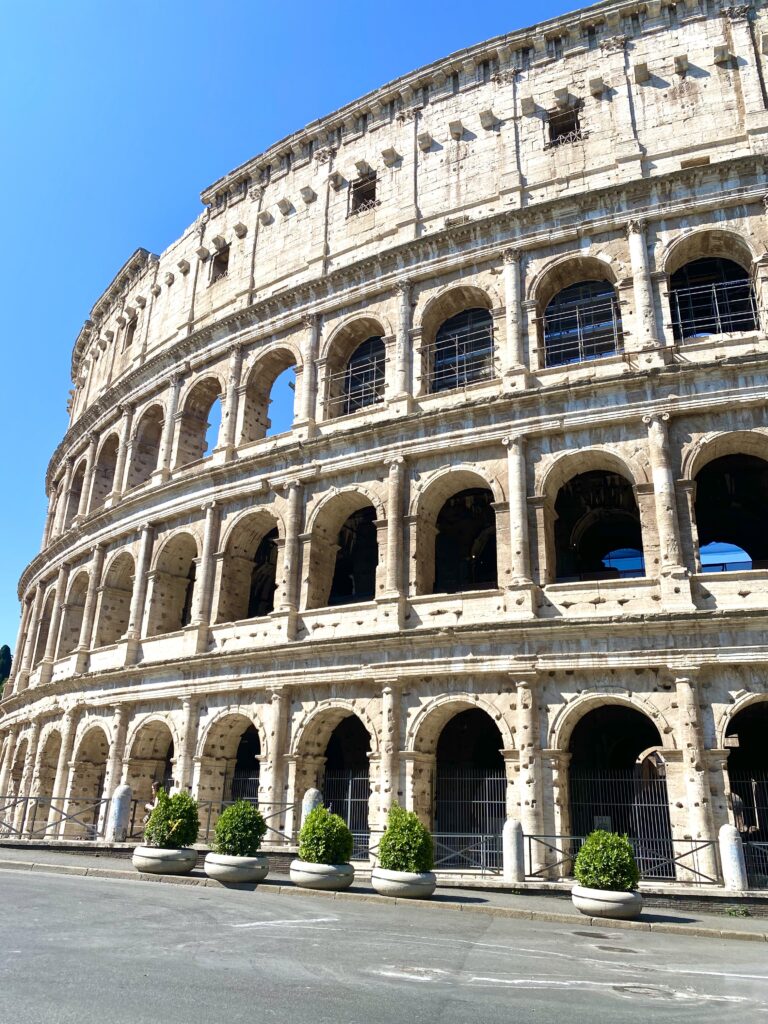The iconic Colosseum in Rome, Italy, shown in striking detail with its ancient arches and weathered stone, under a brilliant blue sky, symbolizing the enduring legacy of Roman architecture and history
