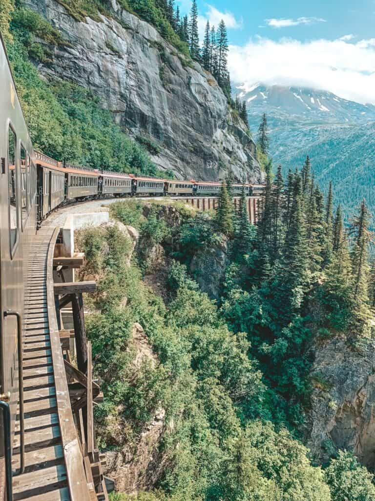 View from the iconic White Pass train in Skagway, Alaska, winding through dramatic mountain landscapes and lush greenery, a snapshot made for Instagram that echoes the allure of historic rail adventures