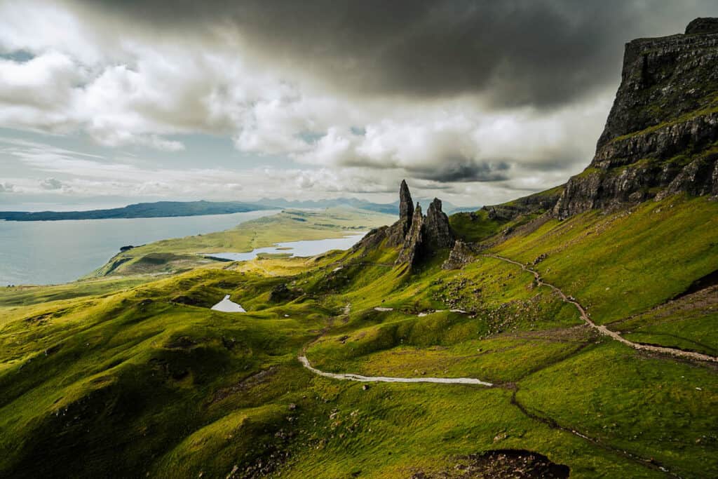 Dramatic landscape of the Old Man of Storr on the Isle of Skye, Scotland, with rugged green hills and the famous pinnacle rock formations standing under a brooding sky, overlooking the serene waters of the Sound of Raasay.