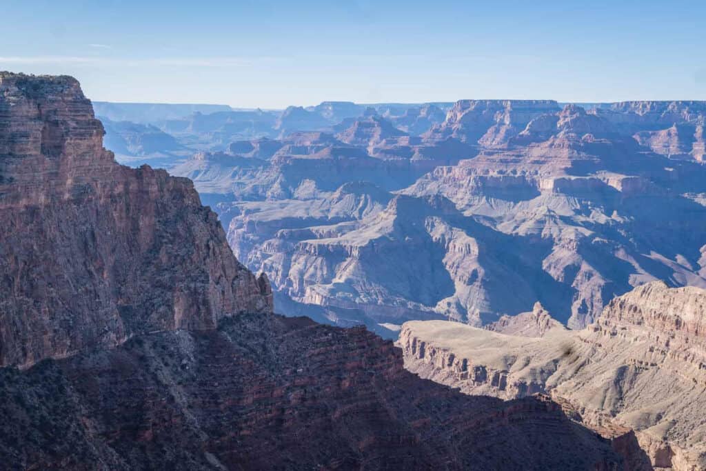 Breathtaking view of the Grand Canyon's expansive, layered rock formations, with deep canyons and cliffs under a clear, vast sky, illustrating the natural wonder's grandeur and the scale of geological time.