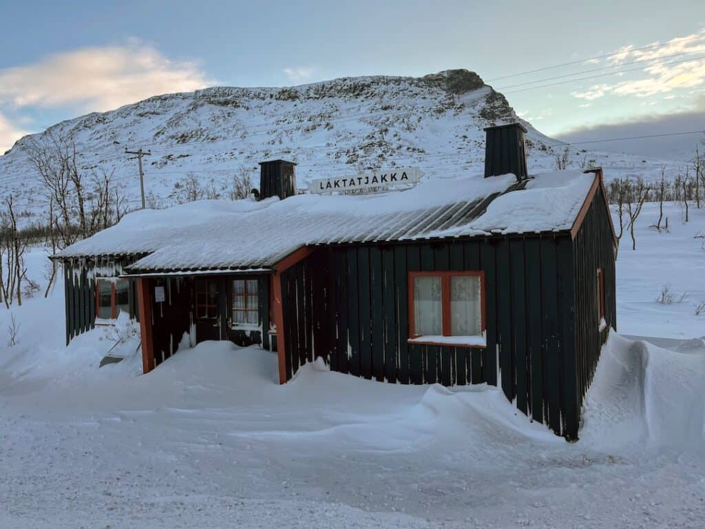 This image shows a small, snow-covered cabin in Abisko, Sweden, with the sign 