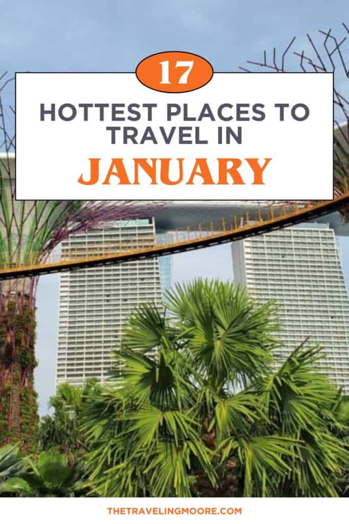 This image is a travel-themed graphic featuring the title "17 Hottest Places to Travel in January" in bold text. The background shows a view of Gardens by the Bay in Singapore, with the famous Supertree Grove and Marina Bay Sands hotel visible. The text is presented in contrasting dark grey and bright orange, while the website "thetravelingmoore.com" is displayed at the bottom. This visually appealing graphic is designed to attract readers looking for travel destinations in January.