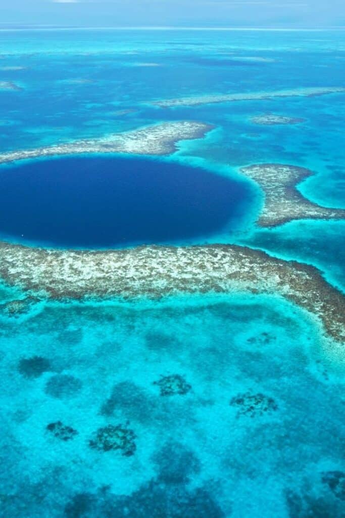 Blue Hole water feature in belize where a dark blue area is surrounded by small land formations and lighter blue water