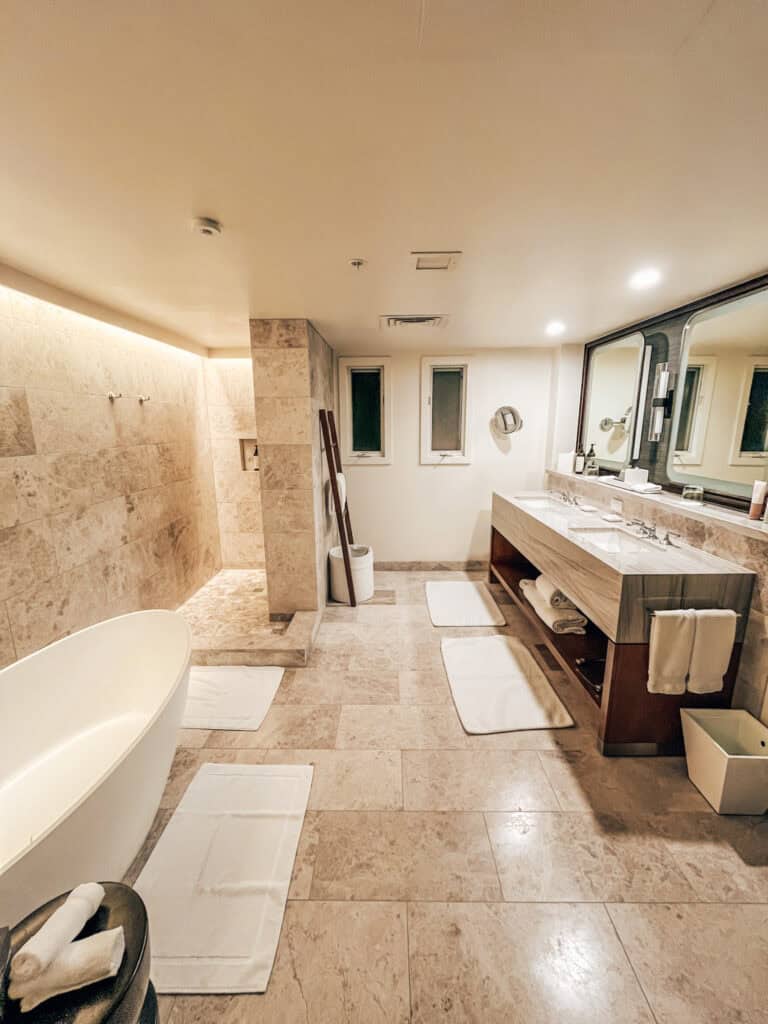 The third image displays a spacious, elegant bathroom with a freestanding tub, large walk-in shower, and dual vanity. The room features light stone flooring and walls, complemented by ambient lighting, creating a spa-like atmosphere.